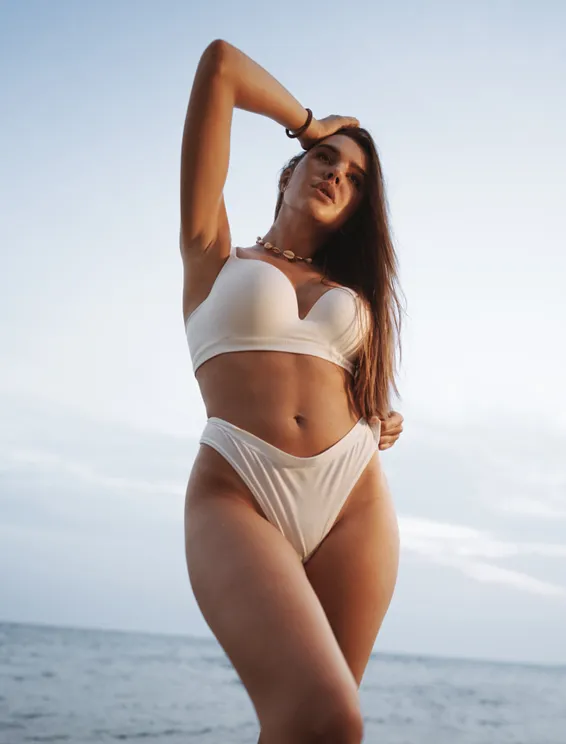 Brunette in white bikini next to ocean - Labiaplasty