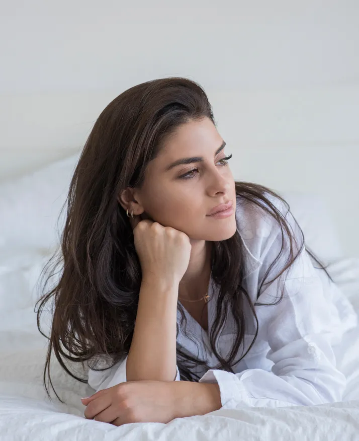 Woman lying on bed resting head on fist - BOTOX