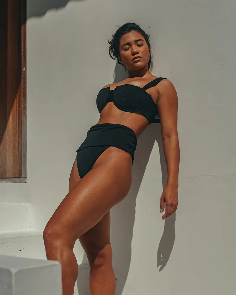 Woman in black bikini with back against wall - Tummy Tuck